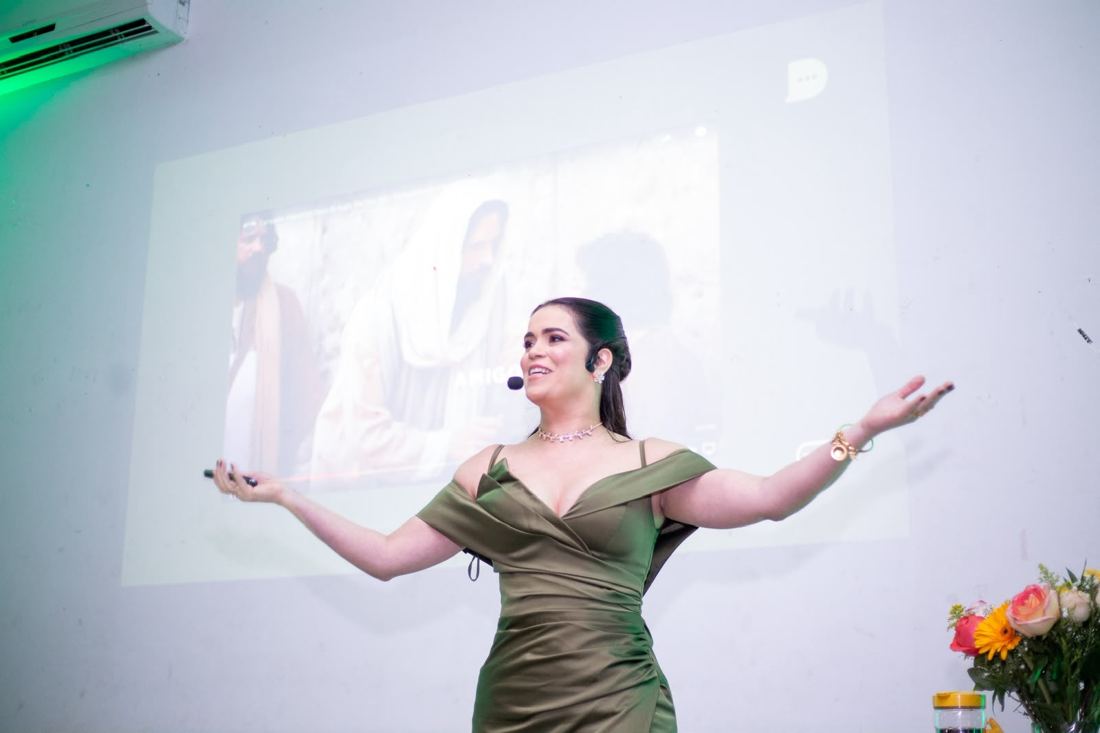 Daniela Milhazes no palco, de braços abertos, durante uma palestra